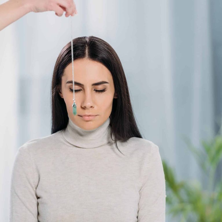 cropped shot of hypnotist with pendulum hypnotizing young woman with closed eyes